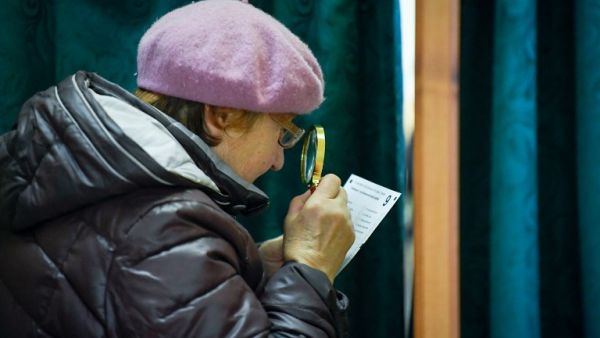 An elderly woman uses a magnifying glass to read her ballot papers as she prepares to cast her ballot at a polling station in Ogre, Latvia, during general elections on October 6, 2018. 
Ilmars ZNOTINS / afp