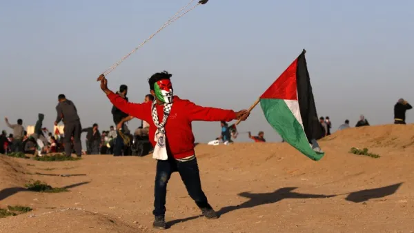 A young Palestinian protester, wearing a Guy Fawkes mask painted in the colours of the Palestinian flag and holding a Palestinian flag in his hand, uses a slingshot to hurl objects during clashes in Gaza . (AFP)