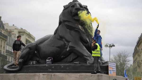 A man holds a flare on the Belfort Lion statue on the Denfert-Rochereau square in Paris, during an anti-government demonstration called by the "Yellow Vest". (Eric FEFERBERG / AFP)
