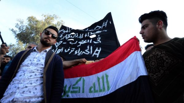 Iraqis wave a national flag alongside a banner mourning the victims of a capsized ferry during a vigil in the northern Iraqi city of Mosul on March 22, 2019. (AFP/ File)