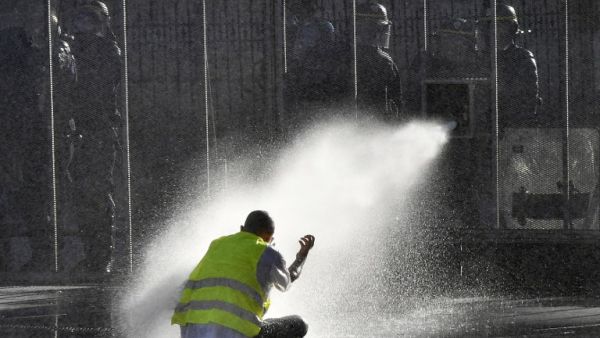 A protester sits on the ground while riot police uses a water cannon during an anti-government demonstration called by the 'Yellow Vest' movement, in Bordeaux, southwestern France, on March 23, 2019. (AFP/ File)