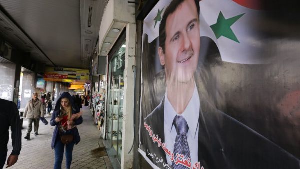 Syrians walk past a portrait of President Bashar al-Assad in the capital Damascus on March 15, 2016. (AFP/Louai Beshara)
