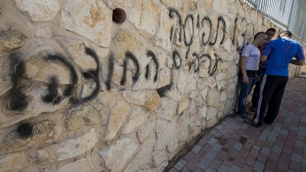 Arab Israeli men stand next to graffiti reading in Hebrew "Arabs Out" on the wall of a mosque in the northern Israeli city of Umm al-Faham on April 18, 2014 (JACK GUEZ / AFP)