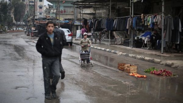 Syrians walk in the rain past a shop in the town of Kfar Batna, on the outskirts of the capital Damascus, November 17, 2015. (AFP/File)