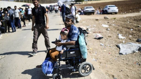 A Syrian refugee on a wheelchair waits on August 28, 2017 at the Oncupinar crossing gate, close to the town of Kilis, south central Turkey, as they wait to cross to Syria for the Eid al-Adha Muslim holiday. Turkish authorities allow Syrian refugees to visit their country for Eid-Al-Adha (Feast of the Sacrifice) celebrities. (AFP)