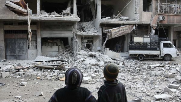 Syrian children look at a building that was damaged in a missile attack on the rebel-held besieged town of Arbin, in the eastern Ghouta region on the outskirts of the capital Damascus, on Jan. 18, 2018 (ABDULMONAM EASSA / AFP)