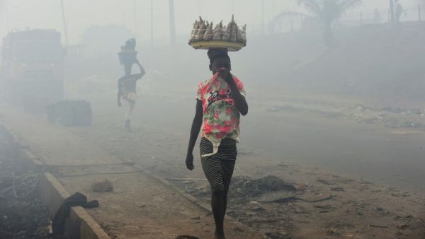Vendors cover their nose as they walk through smoke emanating from the Olusosun dump site in Lagos, Nigeria (AFP/File Photo)
