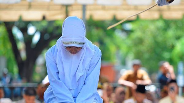 The young woman clenches her fists in anticipation as the cane is brought down across her back (AFP)