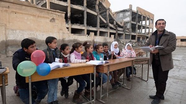 Haunted by the past: A bombed building used as an Isis prison is the backdrop to head Ibrahim Ismail’s talk with pupils (dailymail)