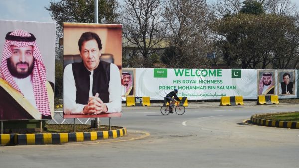 A foreigner rides past billboards showing portraits of Saudi Arabian Crown Prince Mohammed bin Salman (L) and Pakistan's Prime Minister Imran Khan (R) and a banner welcoming the prince ahead of his arrival in Islamabad  (AFP)