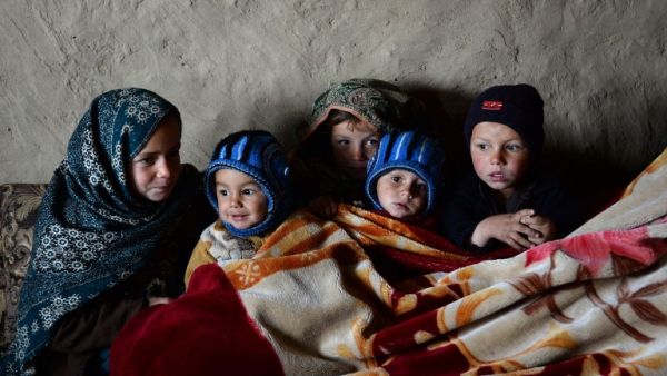 In this photograph taken on January 18, 2017, Afghan children warm themselves with a blanket inside a mud house at a refugee camp on the outskirts of Laghman.  (AFP/Noorullah Shirzada)