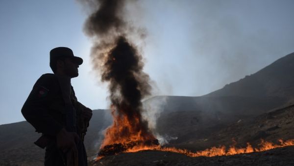 An Afghan policeman watches as a cache of alcohol and drugs burns on the outskirts of Kabul on December 20, 2016. (AFP/Shah Marai)