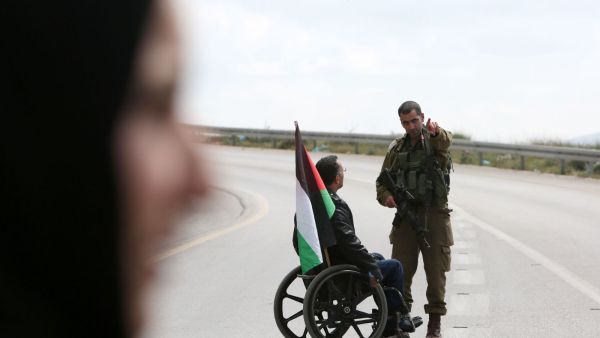A Palestinian protester on a wheelchair talks with an Israeli soldier during clashes (AFP/file) 