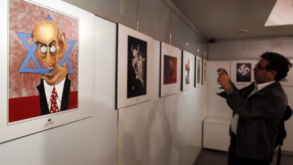 An Iranian man takes a photo of an anti-Israel cartoon displayed at the second international exhibition of drawing and cartoons on the Holocaust in Tehran on May 14, 2016. (AFP/Atta Kenare)