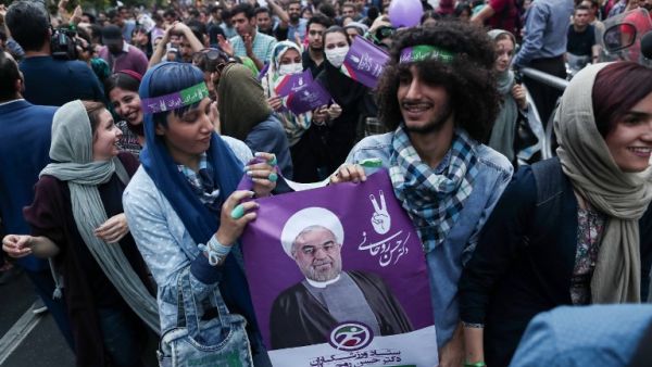 Supporters of newly re-elected Iranian President Hassan Rouhani hold a placard bearing a portrait of him as they take to the streets to celebrate his victory in downtown Tehran on May 20, 2017. (AFP/Behrouz Mehri)