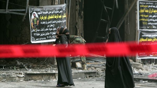 Iraqi women walk past the site of Sunday's bombing, marked off with red tape. (AFP/Sabah Arar)