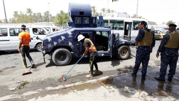 Iraqi workers clean the pavement as security forces stand guard at the site of a suicide bombing on July 24, 2016 near a checkpoint in the Kadhimiyah area, home to a major Shia shrine, in northern Baghdad. (AFP/Sabah Arar)