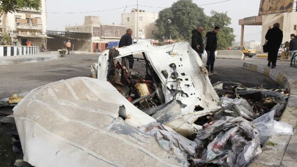 Iraqis walk past the wreckage of a vehicle in the aftermath of a bomb explosion in Baghdad's Al-Karkh district on December 4, 2016. (AFP/Sabah Arar)