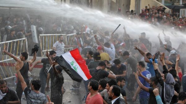 Iraqi protesters chanting slogans and waving national flags are sprayed with water cannon by security forces in clashes in protests against unemployment and lack of basic services Baghdad's Tahrir Square on July 20, 2018. (AFP/Ahmad Al-Rubaye)

