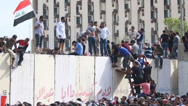 Iraqi protesters climb over a concrete wall surrounding the parliament on April 30.(AFP Photo)
