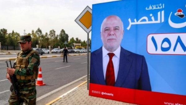 A member of Kurdish security forces stands near a campaign poster for Iraqi Prime Minister Haider al-Abadi for the May 12 parliamentary elections. (AFP/ File Photo)