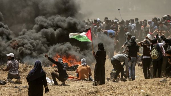 A Palestinian woman holding her national flag looks at clashes with Israeli forces near the border between the Gaza strip and Israel east of Gaza City on May 14, 2018. (MAHMUD HAMS/ AFP)