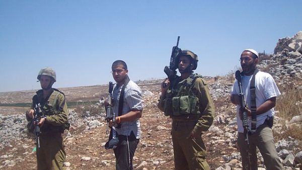 Armed Israeli settlers stand beside IDF soldiers in 2009 (Wikimedia Commons)