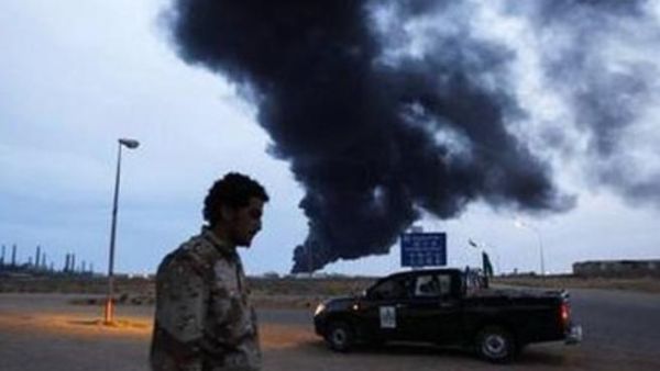 احد انصار القذافي يمر امام نقطة تفتيش قرب طرابلس وتبدو سحابة من الدخان تتصاعد من دبابة تعرضت للقصف