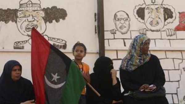 ليبيات يجلسن بالقرب من رسومات للعقيد الليبي معمر القذافي في بنغازي