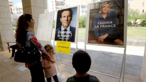 French citizens residing in Lebanon look at the election posters of independent centrist French presidential candidate Emmanuel Macron (L) and far-right Front National (FN - National Front) candidate Marine Le Pen, as they arrive to cast their votes at the French embassy in Beirut on May 7, 2017 during the second round of the French presidential vote. (AFP/Anwar Amro)
