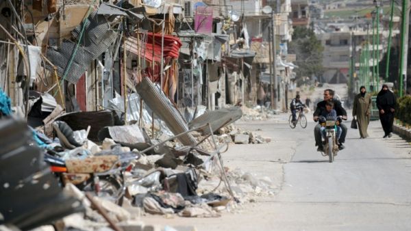 Civilians drive past damaged buildings in Maarat al-Numan, Syria. (AFP/File)