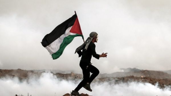 A Palestinian man holds the national flag as he runs through teargas during a protest, on the eastern outskirts of Gaza City, near the border with Israel. (MAHMUD HAMS / AFP)