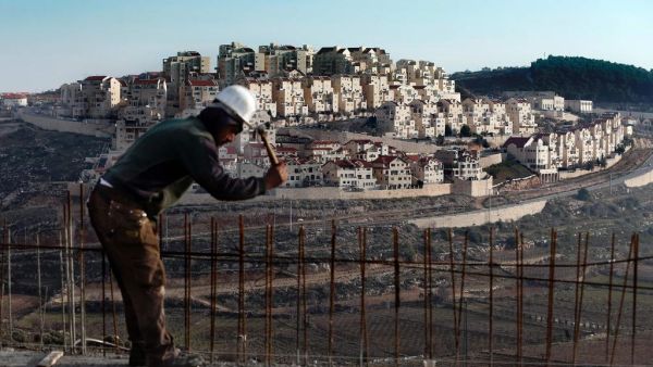 A man works on a construction site in Bethlehem, Palestine, as illegal settlements tower in the distance (AFP / AHMAD GHARABLI)