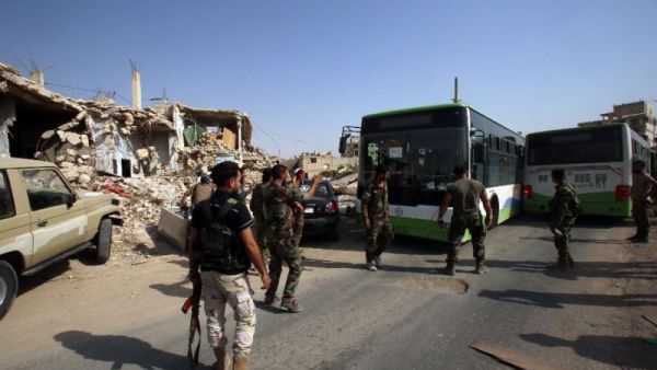 Syrian troops stand guard as a bus carrying people drives by, as part of an evacuation from the town of Daraya outside the capital Damascus on August 26, 2016 (AFP/Youssef Karwashan)