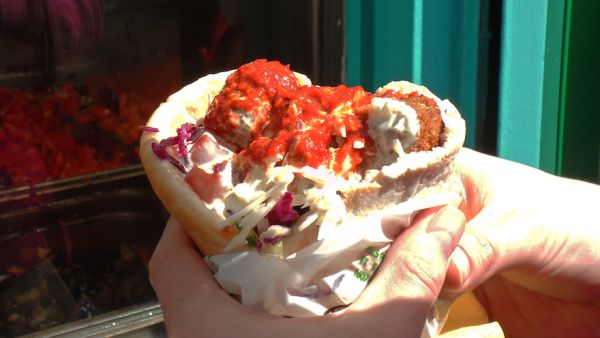 A patron of The Falafel Ace holding the restaurant’s acclaimed falafel sandwich, which is covered in hot sauce. (WikiMedia/Creative Commons)