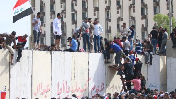 Iraqi protesters climb over a concrete wall surrounding the parliament after breaking into Baghdad. (AFP/File)
