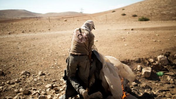 A Palestinian man burns the remains of his previous encampment, in the Jordan Valley settlement of Makhoul September 25, 2013.  The land was closed to Palestinians after Israel declared it a "closed military zone." (Image credit: AFP)