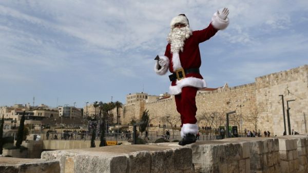 A Palestinian man wears a Santa Claus costume as he walks atop Jerusalem's Old City walls, on December 23, 2016, as Christians around the world prepare to celebrate the holy day. (AFP/Ahmad Gharabli)