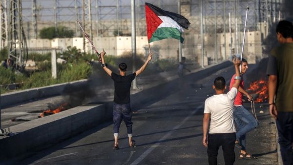 A Palestinian protester holds up a Palestinian flag in one hand while raising a crutch with another during clashes with Israeli forces near Gaza Strip on September 26, 2018.  (SAID KHATIB / AFP)