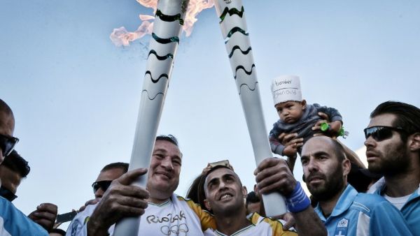 President of the Hellenic Olympic Committee Spyros Kapralos (L) hands over the Olympic Flame to Syrian refugee Ibrahim al-Hussein (C), 27, an amputee swimmer
LOUISA GOULIAMAKI / AFP