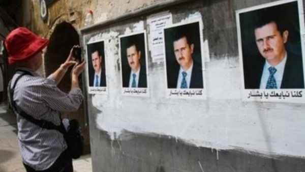 سائحة تلتقط صورا لجدار الصقت عليه صور لبشار الاسد في دمشق