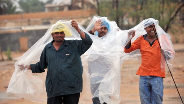 Foreign workers protect themselves from the rain while crossing a flooded street in the Saudi capital Riyadh on November 19, 2013. [AFP]