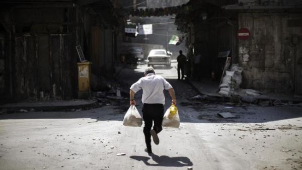 A Syrian man carrying grocery bags tries to dodge sniper fire as he runs through an alley near a checkpoint manned by the Free Syria Army in Aleppo. (AFP/Marco Longari)