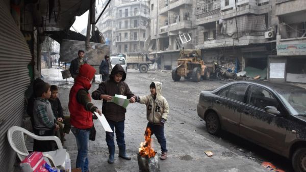 Syrian children gather around a fire as the Syrian government starts to clean up areas formerly held by opposition forces in Aleppo on December 27, 2016, in the Shaar district. (AFP/George Ourfalian)