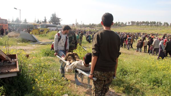 A wounded Syrian, evacuated from government-held Foua and Kefraya, is carried into a field after a car bomb targeted the buses carrying the evacuees. (AFP/Omar Haj Kadour)