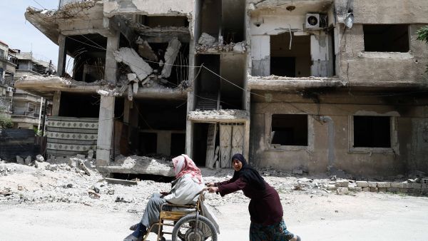 A woman pushes her elderly husband in a wheelchair in opposition-held Hamouria, in the eastern Ghouta region on the outskirts of the capital Damascus on April 26, 2017. (AFP/Abdulmonam Eassa)