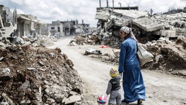 A Kurdish Syrian woman walks with her child past the ruins of the town of Kobane. (AFP/ File Photo)