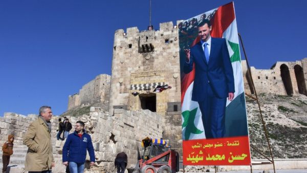 United Nations (UN) High Commissioner for Refugees Filippo Grandi (L) walks past a poster of Syrian President Bashar al-Assad as he visits the old city of the northern Syrian city of Aleppo on February 1, 2017. (AFP/George Ourfalian)