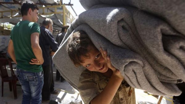 A child in the Syrian town of Douma in the Eastern Ghouta region near Damascus carries blankets distributed by relief workers and the United Nations on July 26, 2018 (AFP/File)
