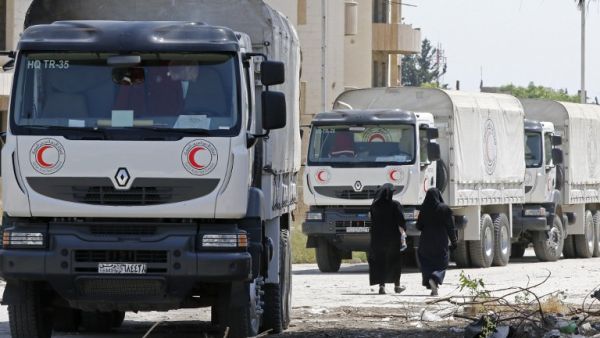 Women walk by Syrian Red Crescent vehicles in Damascus' north eastern al-Qaboun suburb on May 16, 2017, after the formerly rebel-held neighbourhood was retaken by Syrian government forces. (AFP/Louai Beshara)